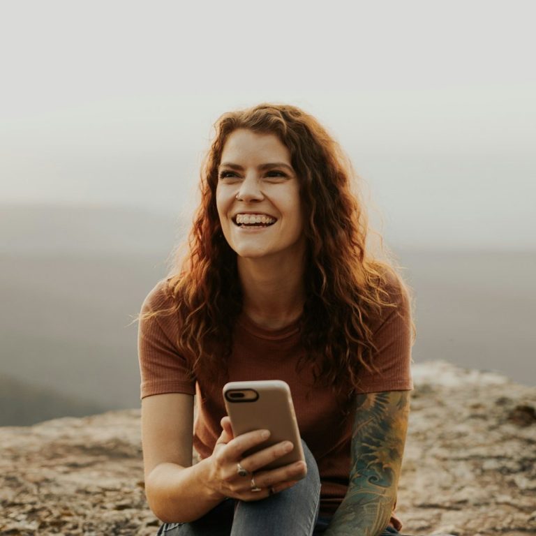 Foto: Junge Frau mit Handy auf einem Stein sitzend als Beispielfoto